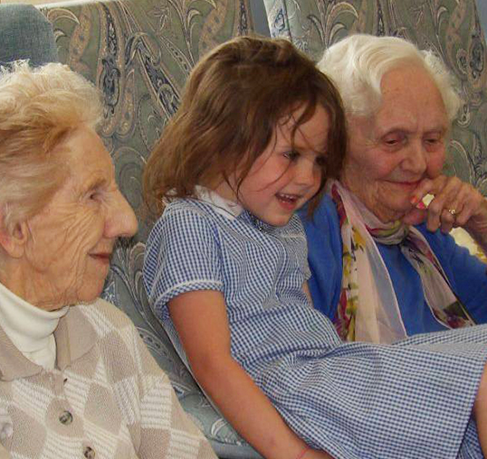 Image shows young school girl sat between two residents, they are all smiling. 